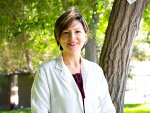Dr. Elena Harrison in white coat holding a stethoscope and smiling at the camera